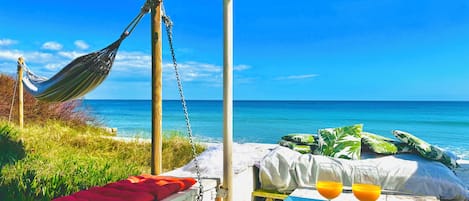 A hammock, a bed with pillows, a table with a tray, and a glass of orange juice.