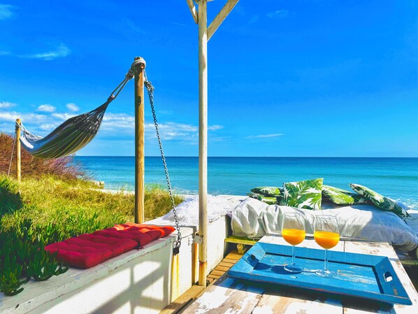 A hammock, a bed with pillows, a table with a tray, and a glass of orange juice.