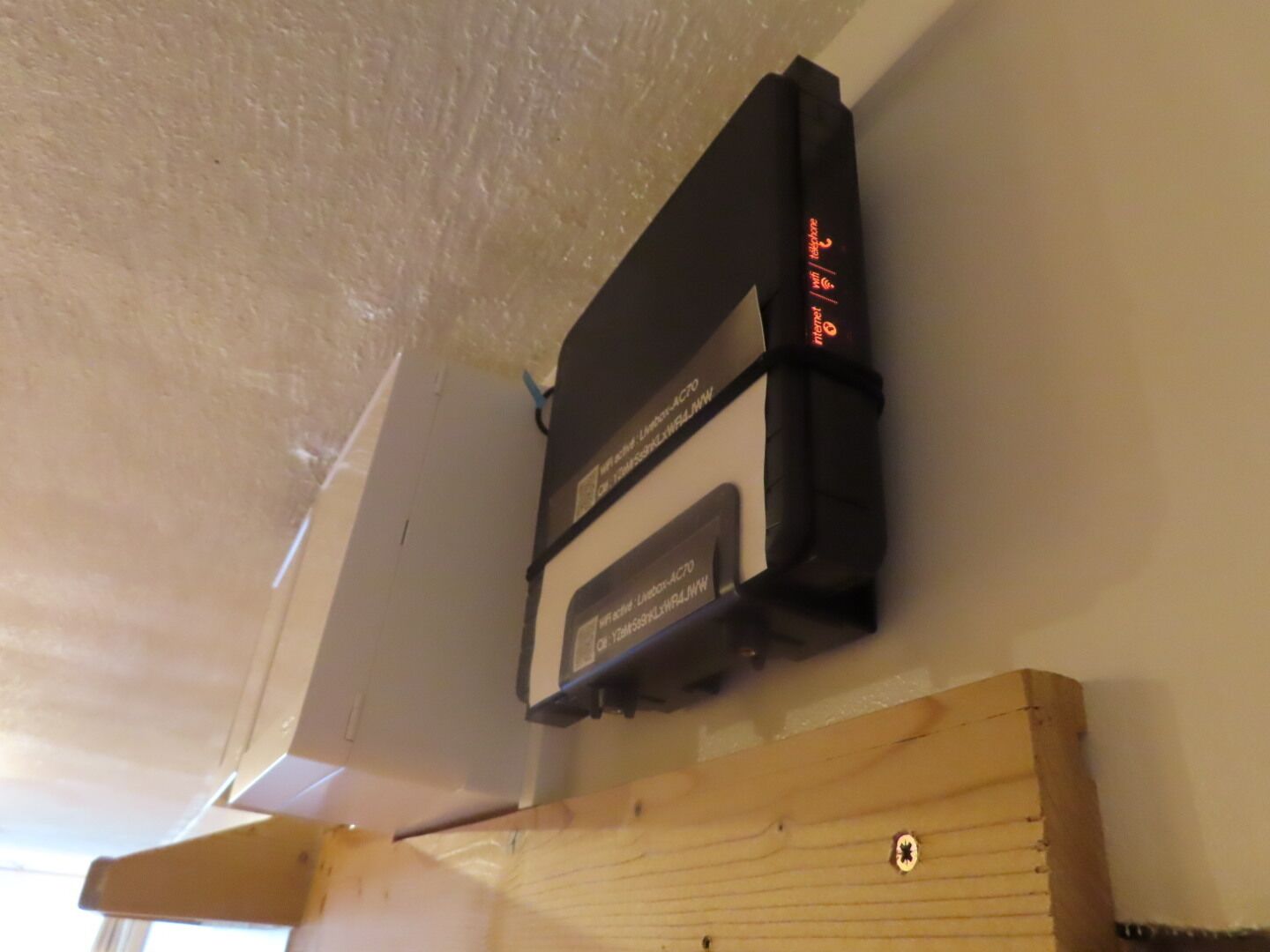 Ein schwarzes elektronisches Gerät an einer Wand befestigt, darunter ein Holzbalken.