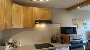A kitchen with wooden cabinets, a built-in stove, a microwave, and a coffee maker. - Roc de Peclet apartment 41 m², South, Foot of the slopes, Heart Station (Les Belleville)