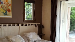 Ein Schlafzimmer mit Bett, Deckenventilator, Fenster mit Blick auf Grünflächen und einem Gemälde an der Wand.