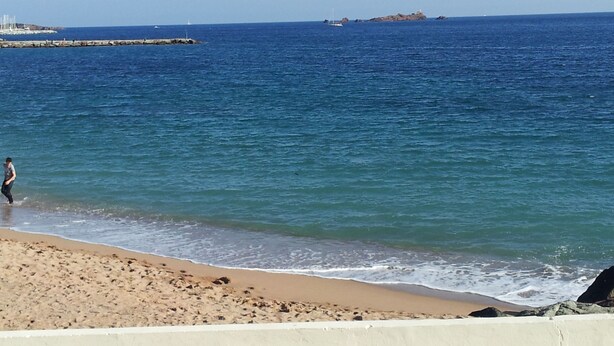 Ein Strand mit einer Person, die am Ufer entlangspaziert, einem Felsen und einer entfernten Insel.