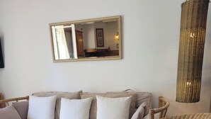 Ein Wohnzimmer mit einer Couch, zwei Korbstühlen, einem runden Tisch, einer hängenden Ampel und einem Spiegel an der Wand.