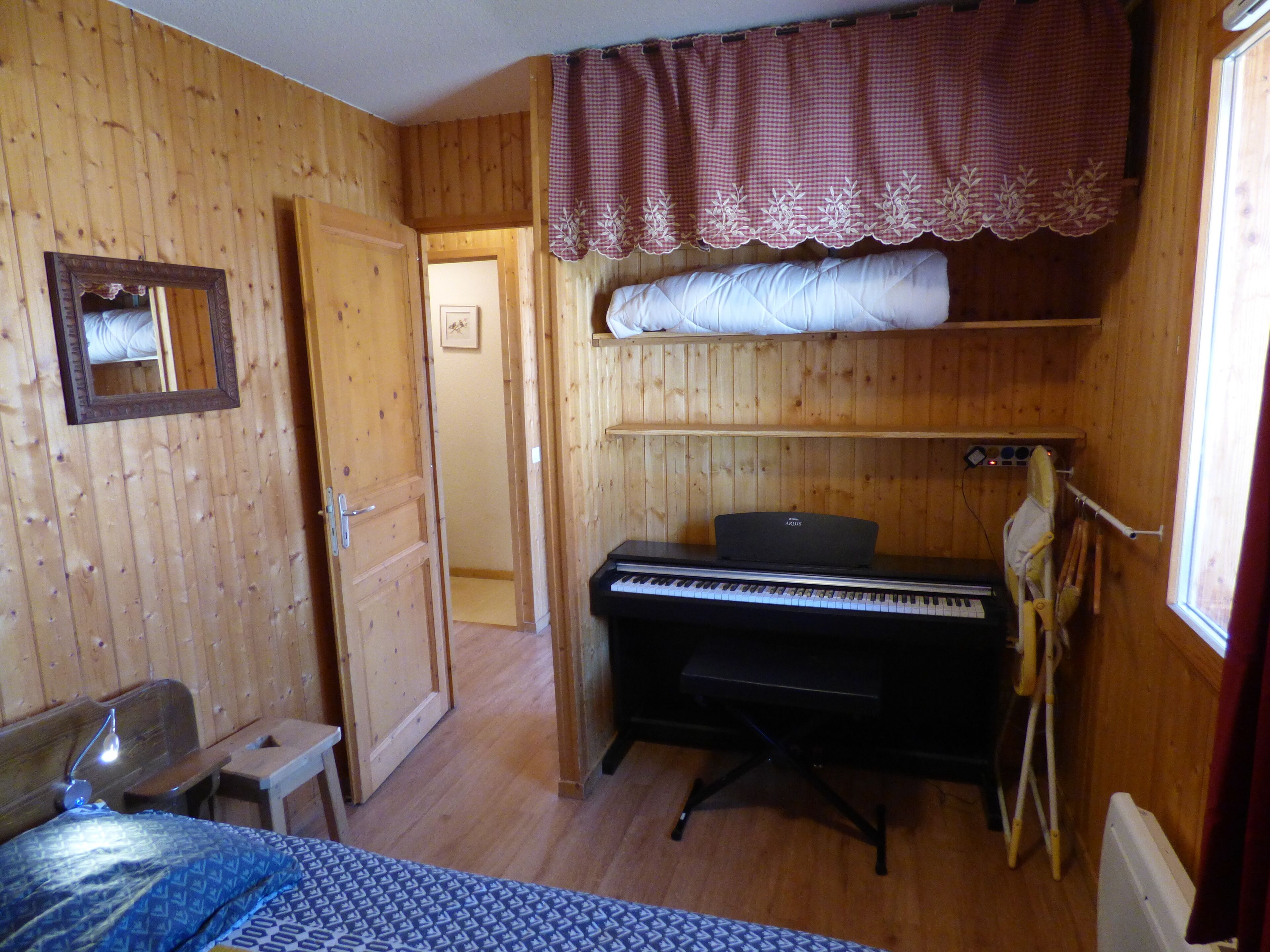 A wooden room with a bed, a piano, and a mirror on the wall.