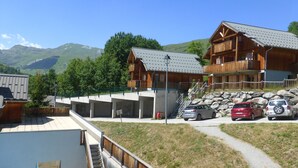 A wooden lodge with a balcony and a staircase leading to a second floor. There are cars parked in front and a path leading to the lodge. - Appart 7 pers au ski, 3*, Saint Jean d'Arves - Les Sybelles - Swimming pool (Saint jean d'arves)