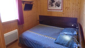 A room with wooden walls, a bed with patterned bedding, a mounted picture, and a window with curtains.