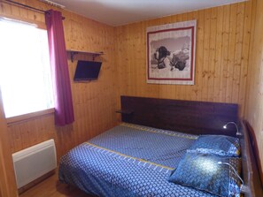 Une pièce aux murs en bois, un lit avec une literie à motifs, un tableau accroché au mur et une fenêtre avec des rideaux.