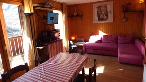 A cozy living room with a wooden interior, a purple sofa, a checkered table, and a television on a wooden shelf. - Appart 7 pers au ski, 3*, Saint Jean d'Arves - Les Sybelles - Swimming pool (Saint jean d'arves)