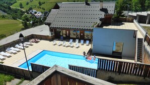 A swimming pool with lounge chairs, a wooden deck, and a view of a mountainous landscape. - Appart 7 pers au ski, 3*, Saint Jean d'Arves - Les Sybelles - Swimming pool (Saint jean d'arves)
