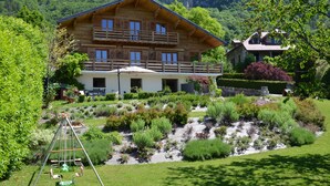 Eine Holzhütte mit Balkon, umgeben von einem gepflegten Garten mit verschiedenen Pflanzen und einer Schaukel.
