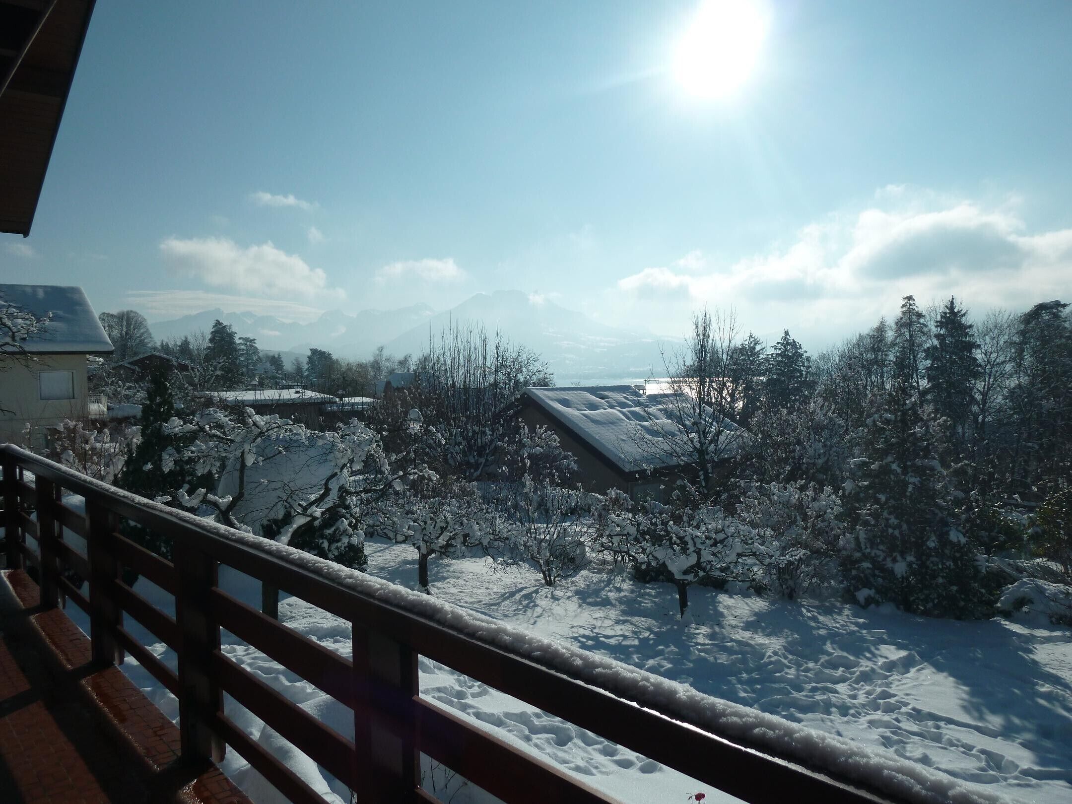 A snowy landscape with a wooden railing, a building with a sloped roof, and a clear sky.
