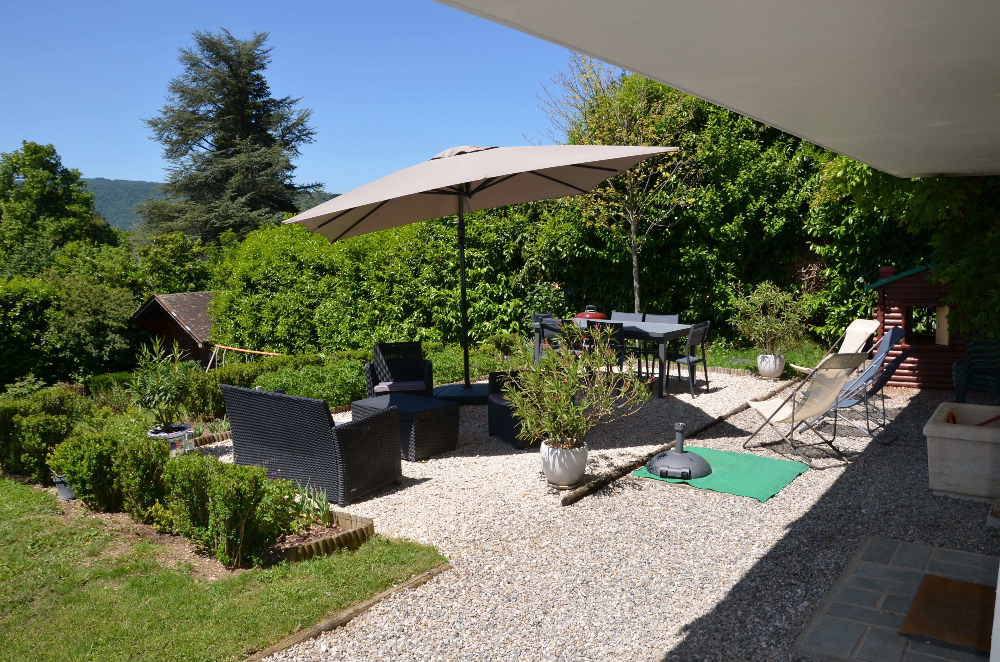 Une terrasse extérieure dotée d’un grand parasol, d’un espace salon et offrant une vue sur une zone boisée.