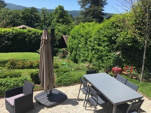 Un patio al aire libre con una mesa y sillas, rodeado por un jardín con una parrilla y un columpio.