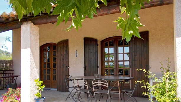Un patio con mesa y sillas, puertas de madera y plantas en macetas.
