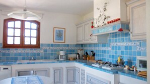 Una cocina con azulejos azules, una ventana, una mesa de comedor y armarios.