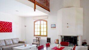 Un salón amplio con techo alto, una zona de comedor con sillas rojas, un sofá y una mesa de centro.