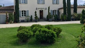 Uma casa de dois andares com telhado de telhas, porta da frente e entrada com calçamento de brita.