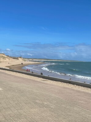 A beach with a paved walkway, sandy dunes, and the ocean.