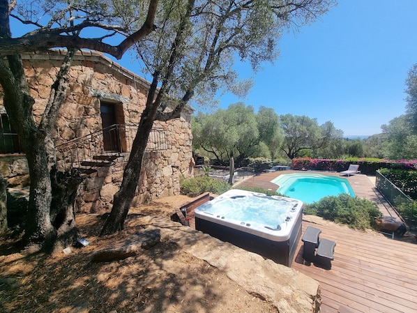 A stone building with a hot tub and a swimming pool, surrounded by trees and a wooden deck.