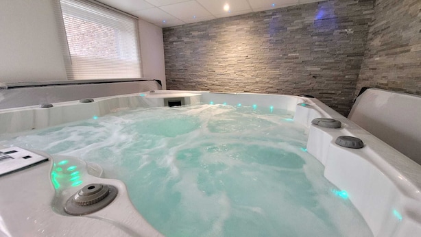 A spa room with a stone wall, a window with blinds, and a hot tub with bubbles. - Contemporary house 10 people with sauna and Spa (Kaysersberg Vignoble)