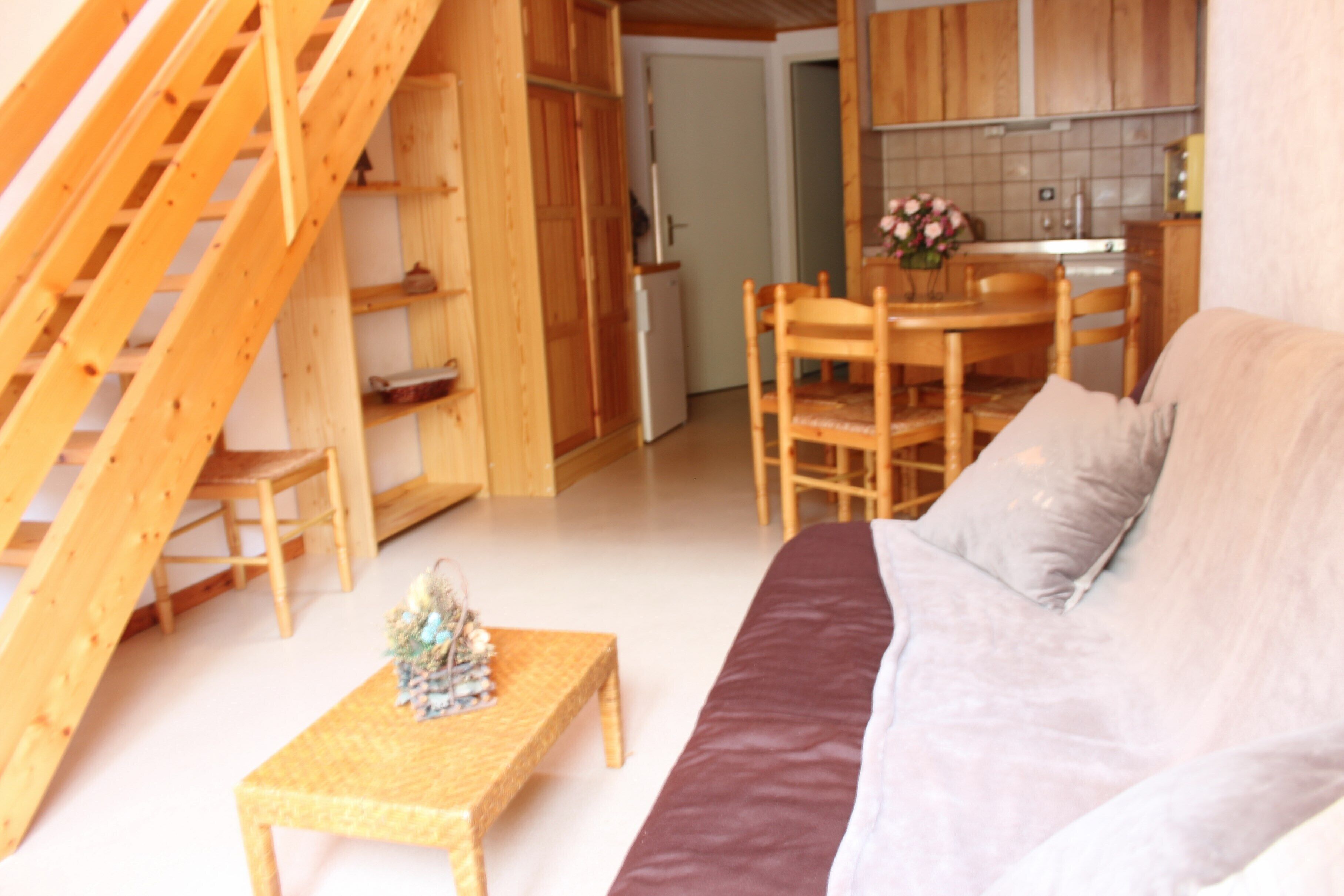 A cozy living room with a wooden staircase, a dining area, and a kitchen.
