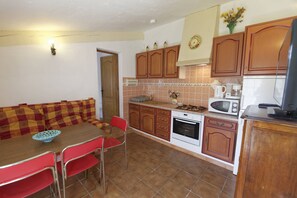 Una cocina compacta con armarios de madera, una mesa de comedor con sillas rojas, un microondas y una estufa.