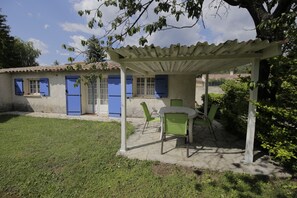 Un patio cubierto con mesa y sillas, una pérgola y una casa con contraventanas azules.