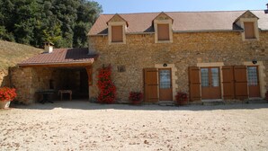 Un bâtiment en pierre avec un toit en tuiles, des volets en bois et une allée gravillonnée.