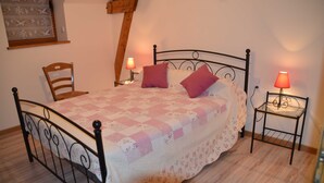 Une chambre à coucher comprenant un lit, deux tables de chevet, une chaise et une structure en poutres apparentes.