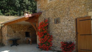 Un bâtiment en pierre avec une porte en bois, une table et des fleurs rouges.
