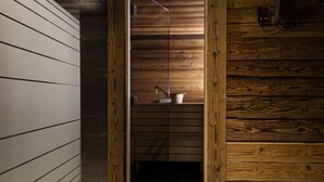 Interieur van een houten blokhut met een houten wand, een metalen plank met een witte container, en een klein elektronisch apparaat aan de wand.