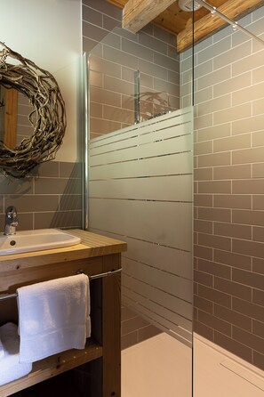 Une salle de bain avec un meuble-lavabo en bois, une cabine de douche en verre et un mur en briques.