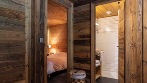 Een houten interieur met een bed, een klein krukje en een badkamer met witte tegels.