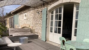 A stone building with a wooden deck, a sofa, and a table with chairs. - Stone farmhouse with swimming pool between Avignon and Orange, in Roquemaure (Roquemaure)