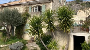 Una casa in pietra con tetto in tegole, un piccolo balcone e un giardino con palme.