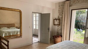 Camera da letto con due letti, una sedia di legno, un cesto in vimini e vista sul giardino attraverso una porta.