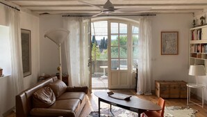 Un accogliente soggiorno con un divano in pelle marrone, un tavolino, una lampada da terra, una libreria e un'ampia finestra con tende.