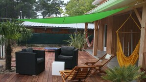 Una terraza de madera con mobiliario exterior, una hamaca y una vela de sombra verde.