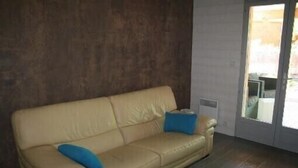 Un sofá de cuero color beige con dos cojines azules, ubicado frente a una pared oscura con puerta corrediza de vidrio que da al exterior.