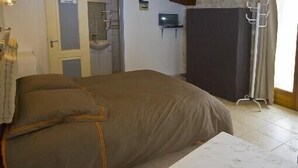 Un dormitori amb un llit, una taula petita, una televisió i un bany visible a través d'una porta oberta.