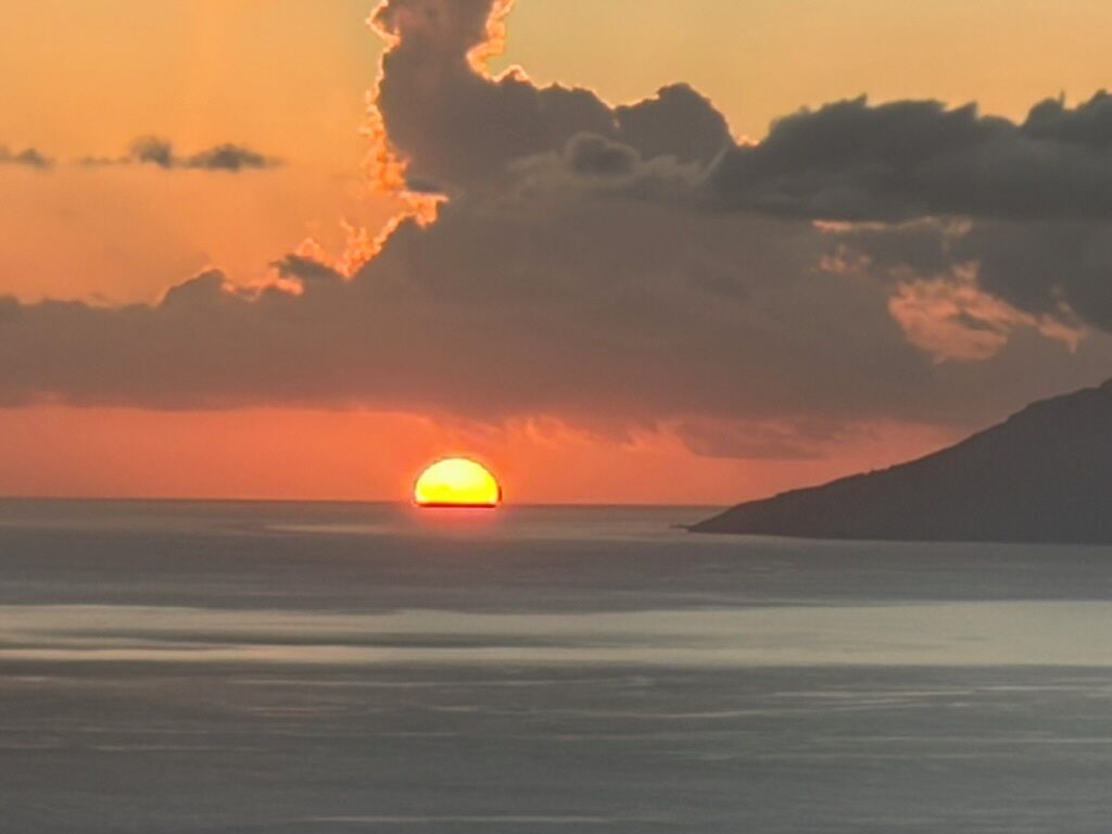 Un coucher de soleil sur une étendue d’eau, avec la silhouette d’une masse terrestre à l’horizon.
