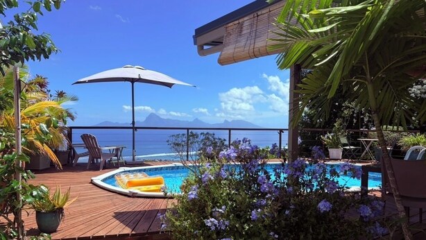 Un espace piscine avec vue sur l’océan, entouré d’une terrasse en bois et agrémenté de plantes en pot.