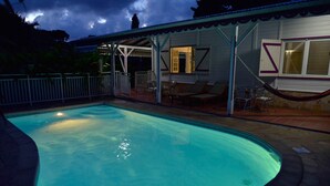 Una piscina con un portico coperto, un'area prendisole recintata e vista sul cielo.