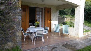 An outdoor patio with a table and chairs, stone walls, and a view of the surrounding garden. - Spacious ground floor of villa, magnificent sea view, terrace , enclosed parking (Le Lavandou)