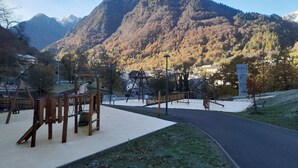 Un parque infantil con estructuras de madera y un sendero pavimentado que lleva a un paisaje montañoso.