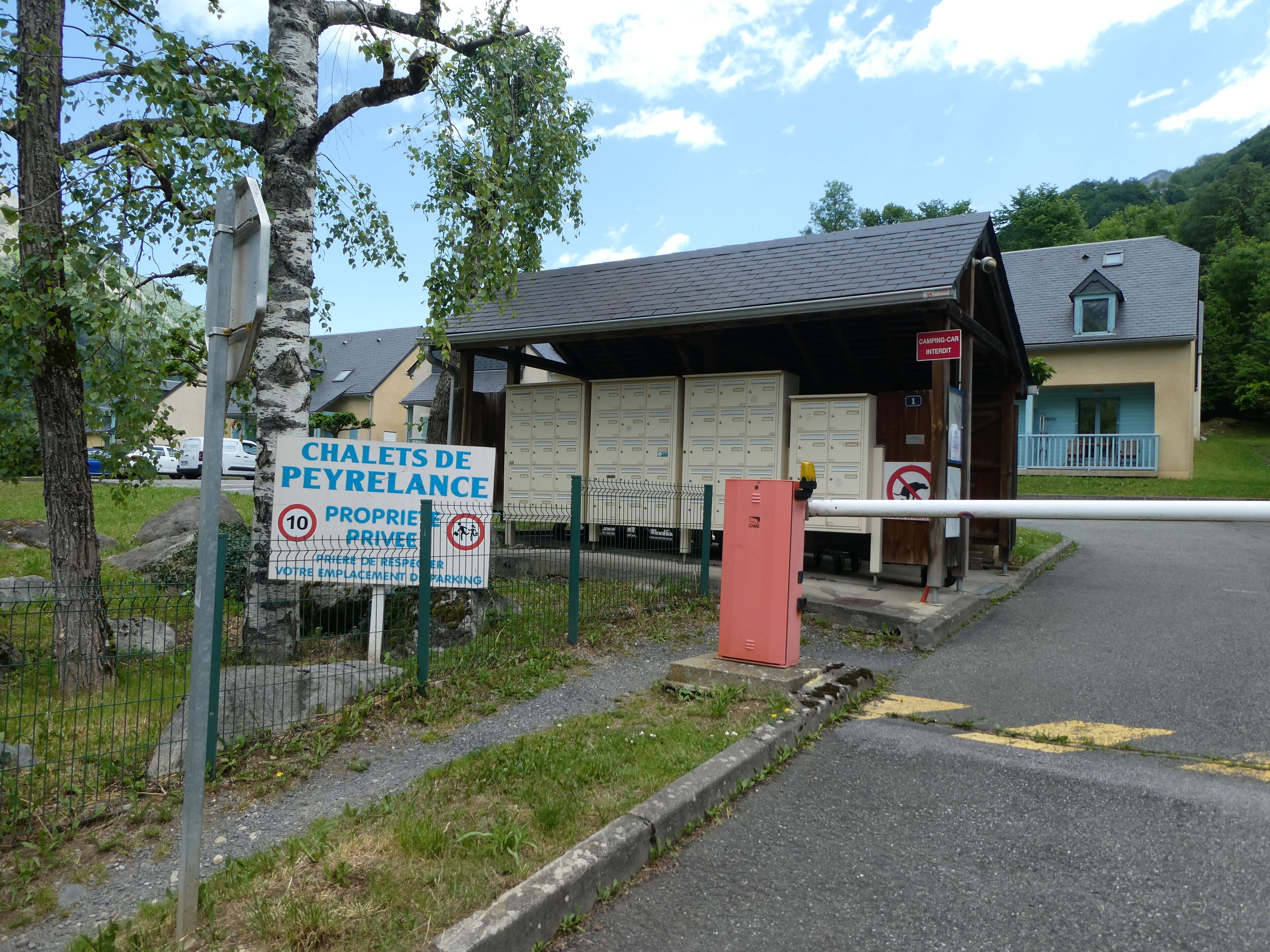 Un área de estacionamiento con acceso restringido, con un cartel que indica 'Chalets de Peyrelance' y un letrero que dice 'Autocaravanas Prohibidas'.