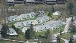Un barrio residencial con varias casas de dos pisos, algunas con balcones, rodeado de follaje y un paisaje montañoso.