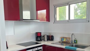 Eine moderne Küche mit roten Schränken, einer Edelstahl-Spüle, einem eingebauten Backofen und einem Fenster über der Spüle.