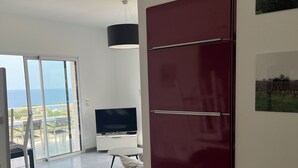 Ein modernes Wohnzimmer mit einem großen Fernseher, einem roten Schrank und Meerblick durch eine Glastür.