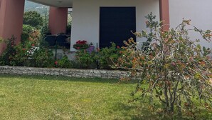 Ein modernes, zweistöckiges Haus mit Balkon, Steinmauer und verschiedenen Kübelpflanzen.